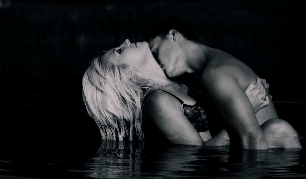 Sensual couple embracing in water at night, showcasing intimacy and romance in a black and white photograph.